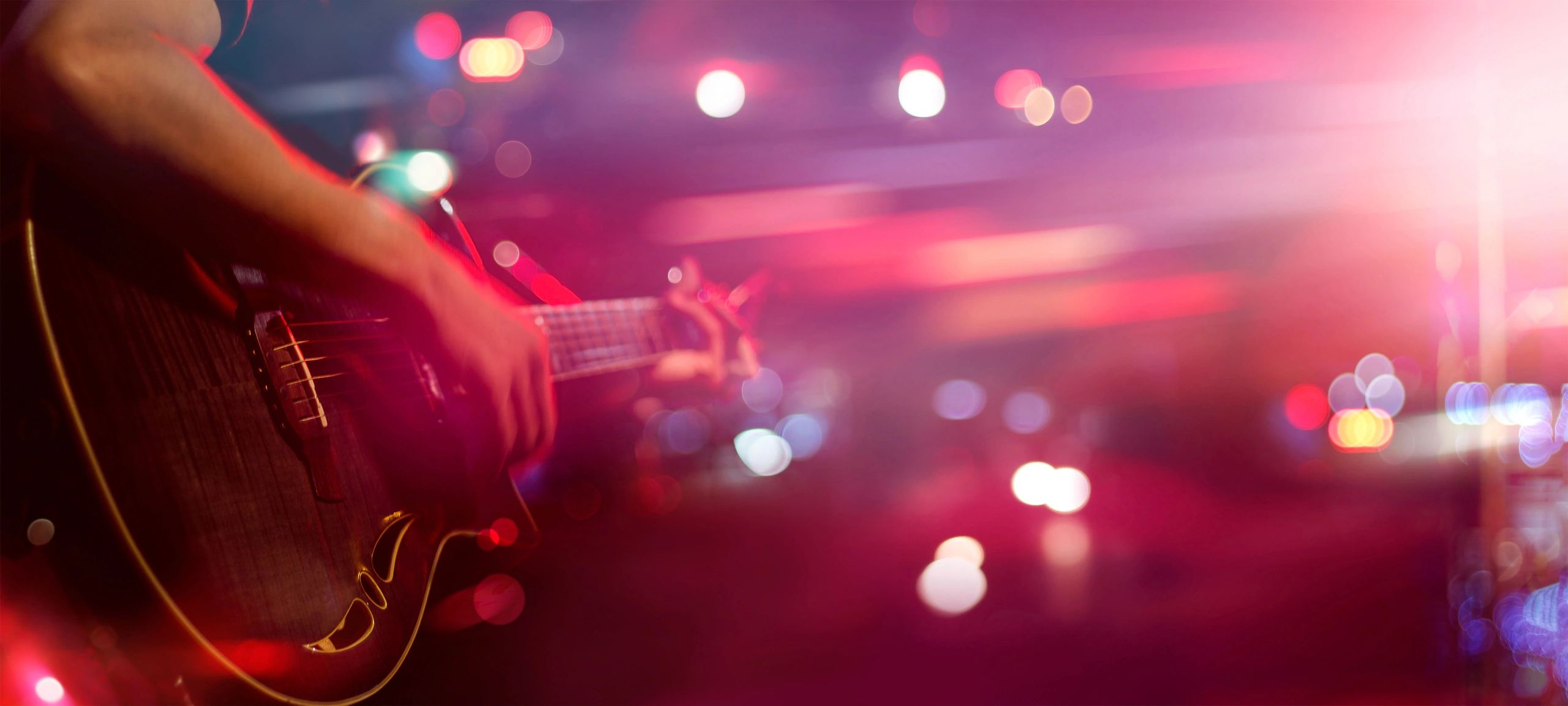 Guitarist playing under vibrant pink and purple stage lights.