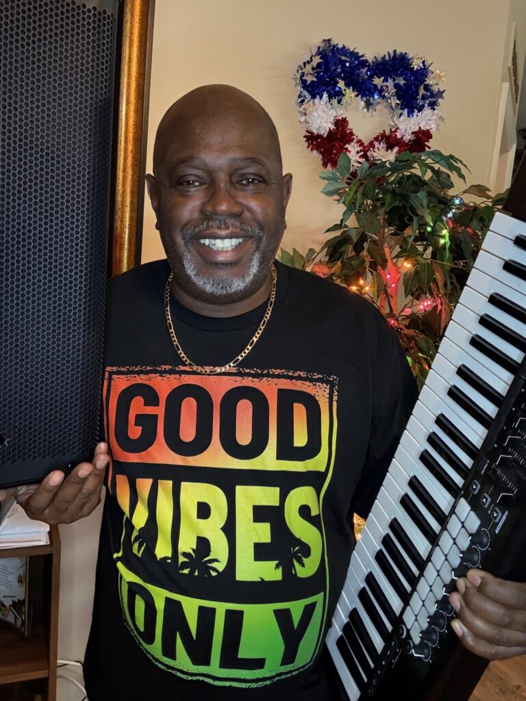 Smiling man holding keyboard and speaker indoors.