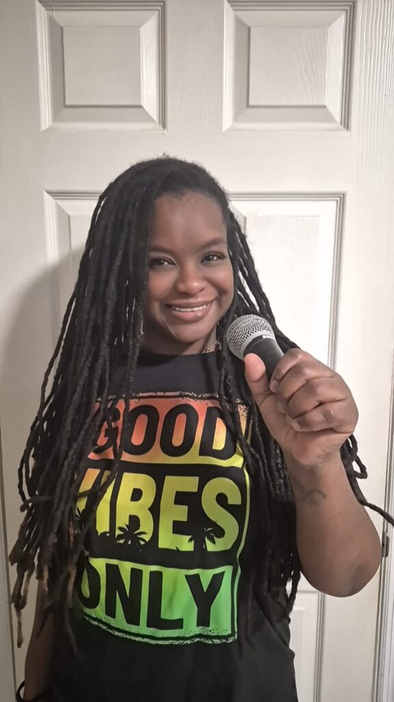 Smiling woman with long braided hair speaking into a microphone.