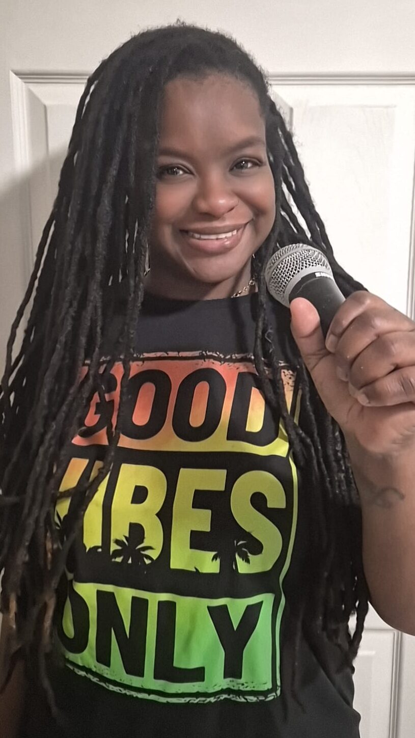 Smiling woman with long braided hair speaking into a microphone.